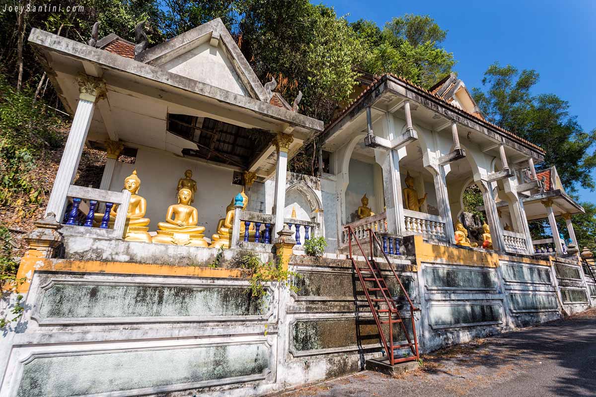 Traditional open-air shrines with golden Buddha statues built along the hillside road of Wat Koh Siray in Phuket