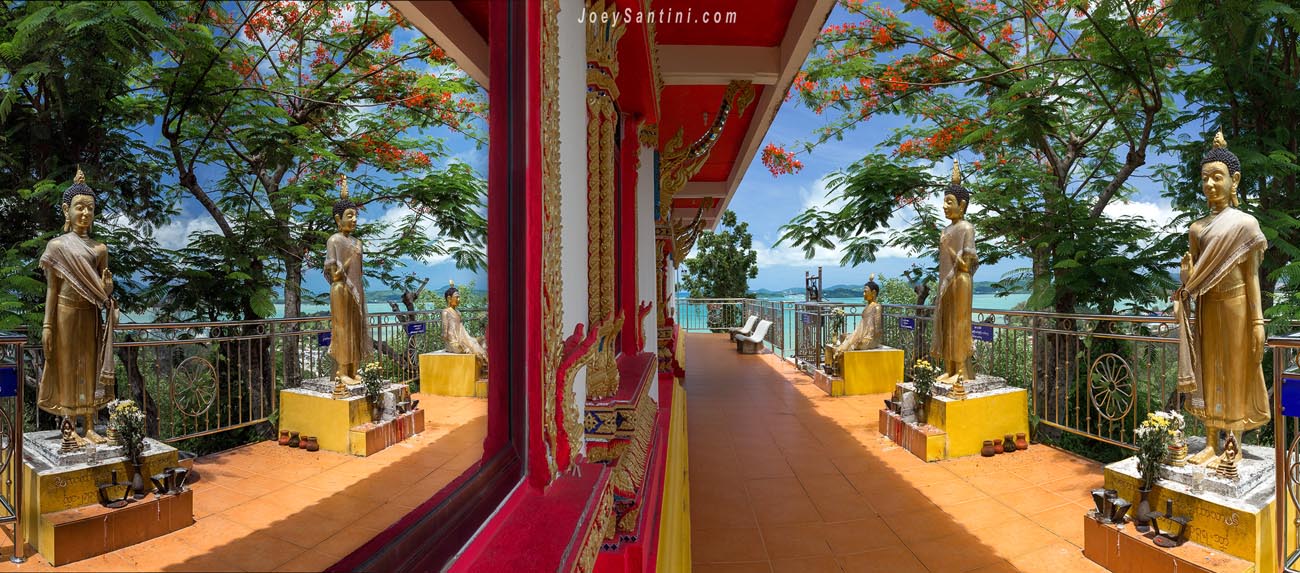 Golden standing Buddha statues along the temple terrace overlooking the sea at Wat Koh Siray