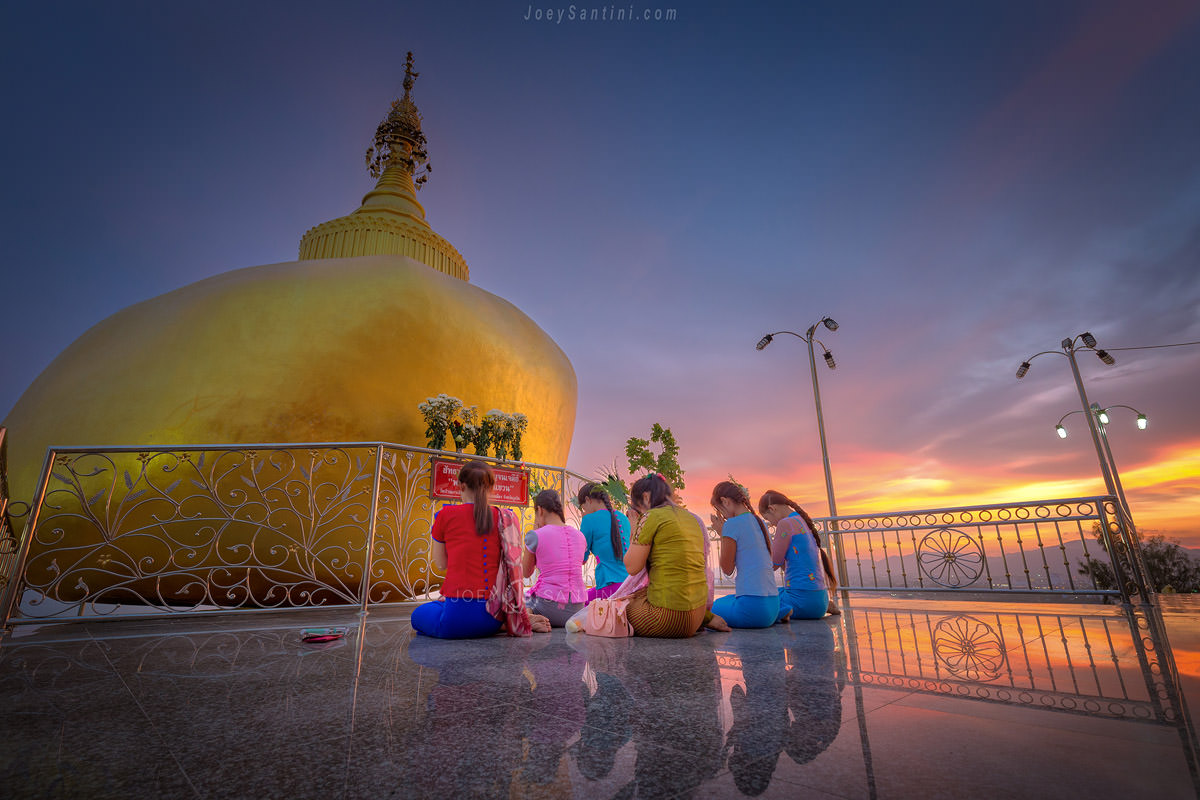 Devotees praying in front of the golden chedi at Wat Koh Siray during a dramatic Phuket sunset