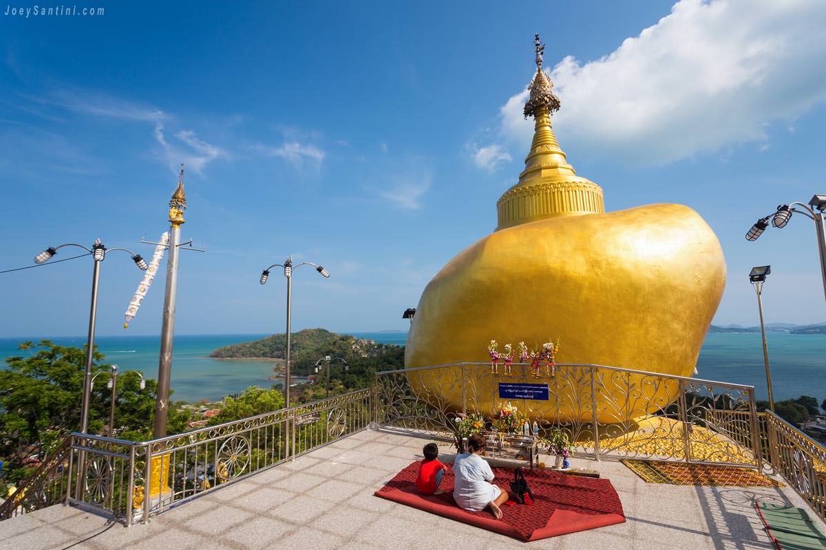 Visitors praying before the golden rock chedi on the terrace at Wat Koh Siray overlooking the Andaman Sea
