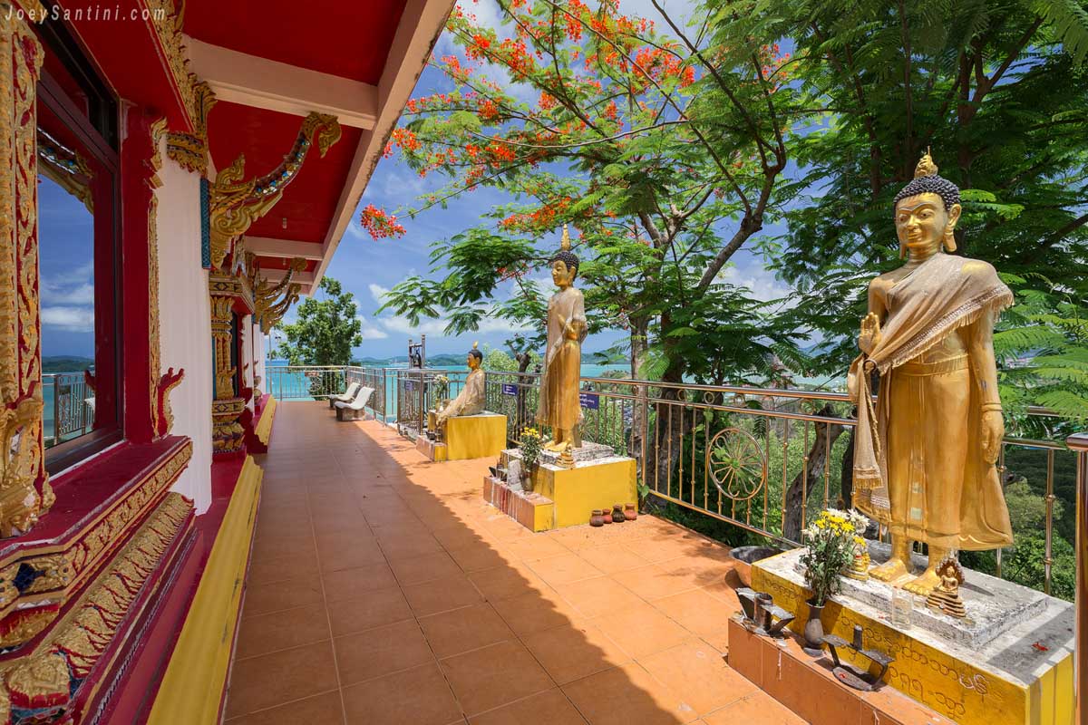 Row of golden standing Buddha statues along the outdoor terrace of Wat Koh Siray overlooking the ocean in Phuket