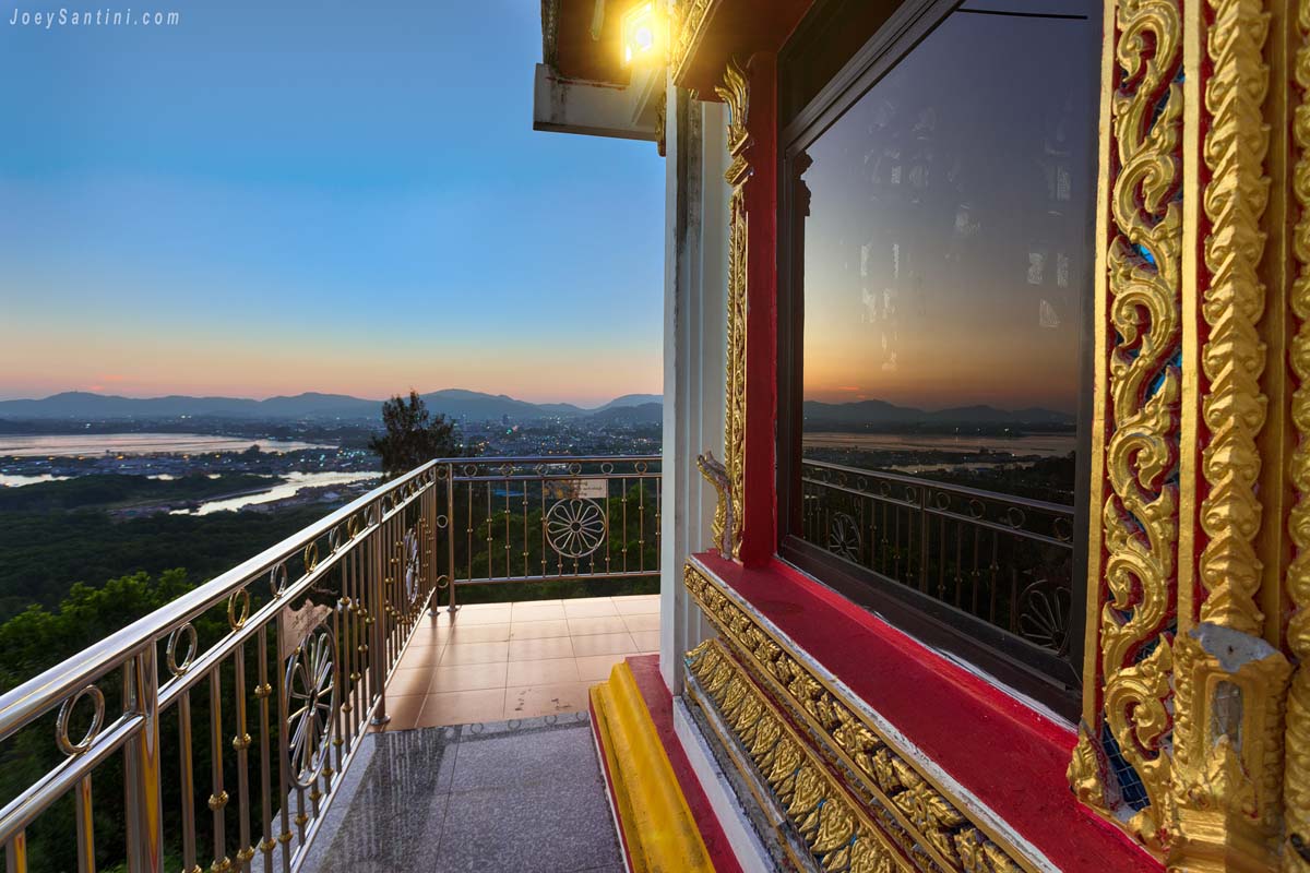 Sunset view over Phuket coastline reflected in the window of Wat Koh Siray temple terrace