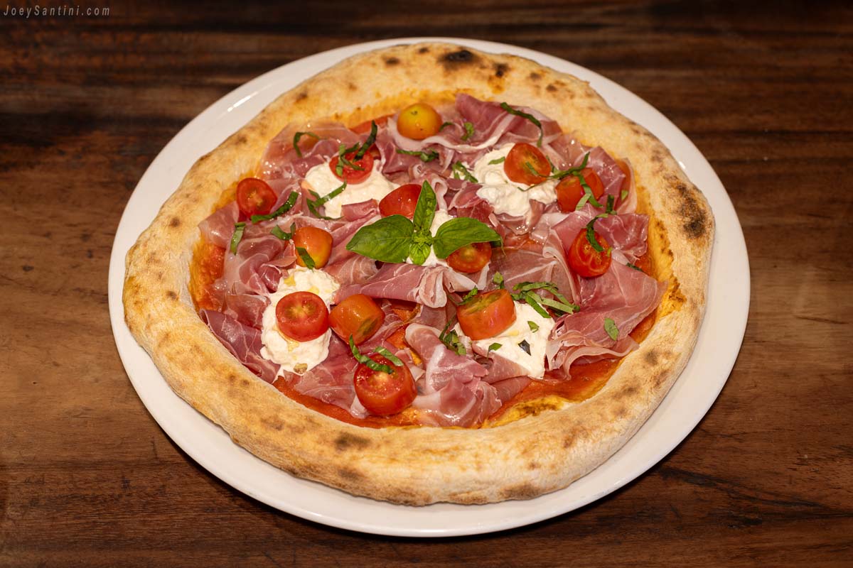 Shot of a pizza with red tomatoes and red Parma ham and green basil leaf.