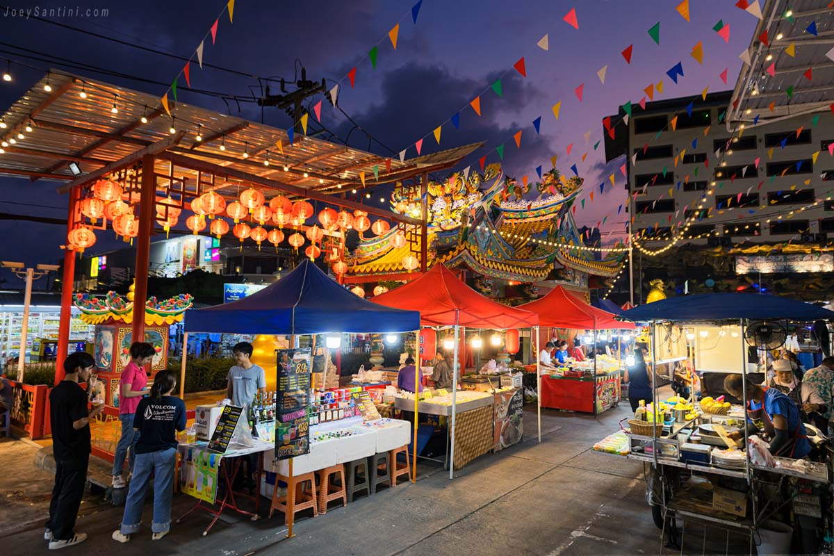 Vibrant Banzaan Night Market in Patong featuring glowing food stalls, colorful pennant banners, and an ornate Thai shrine at dusk