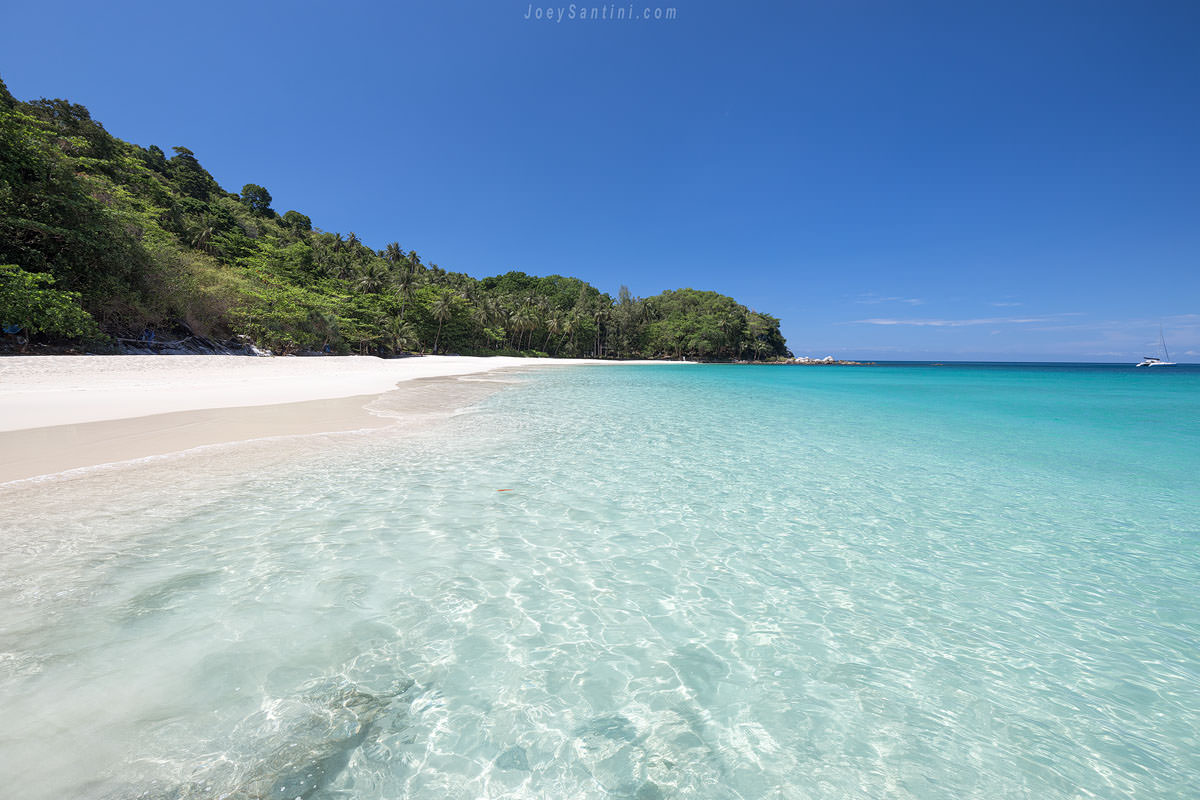 Crystal clear turquoise ocean water washing onto the white sand shore of Freedom Beach in Phuket.