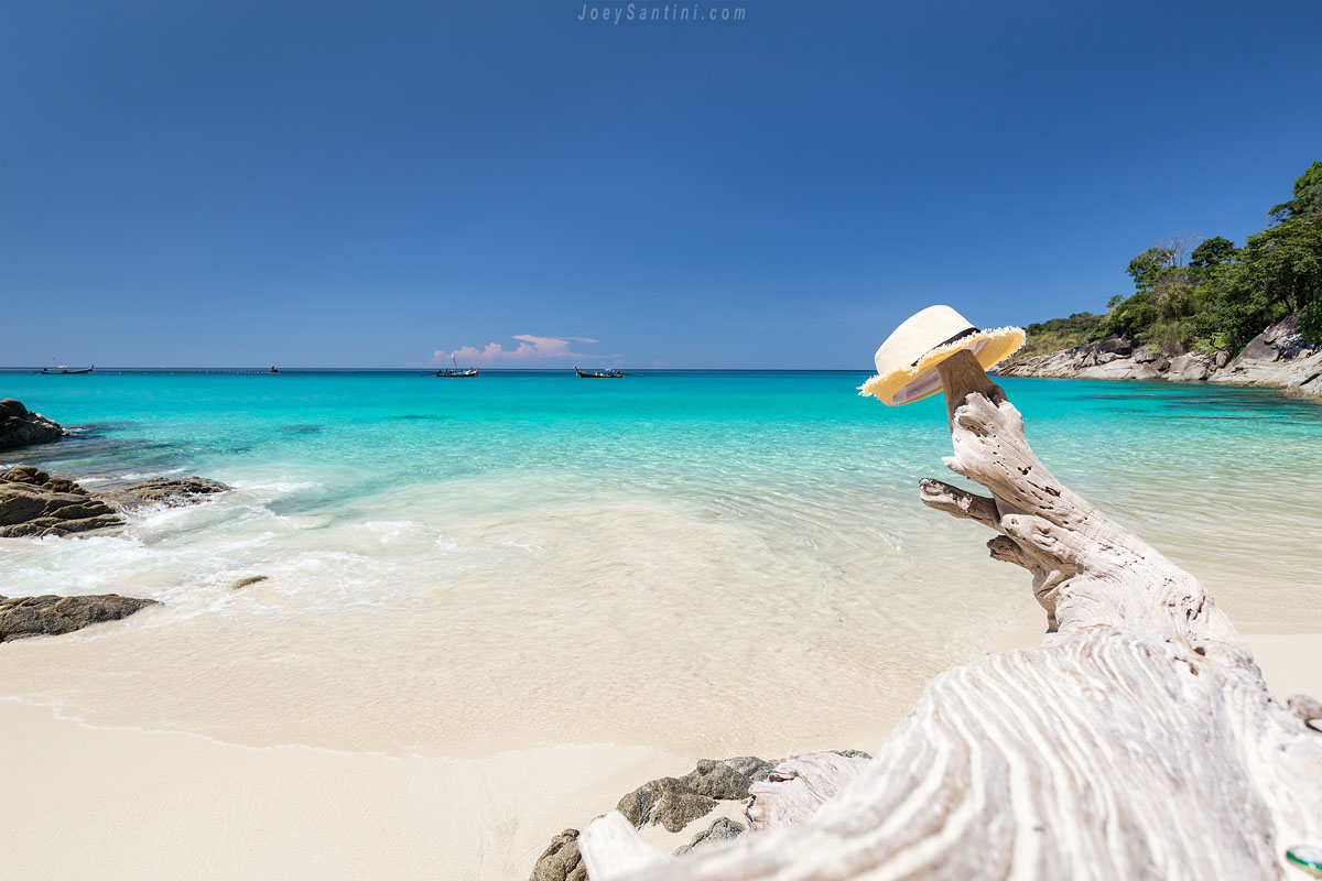 Tropical white sand beach at Freedom Beach with crystal clear turquoise sea and a straw hat on a piece of driftwood in the foreground.