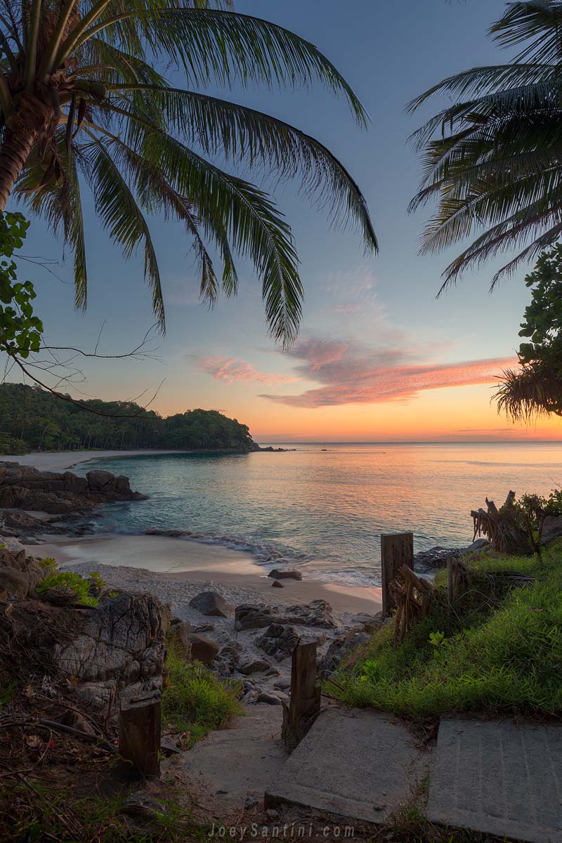 Tropical sunset at Freedom Beach with pink and purple shades in the sky and a palm tree on the right.