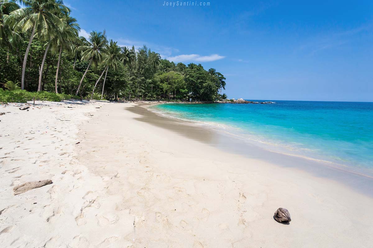Wide deserted white sand beach curving along the clear turquoise sea of Freedom Beach under a blue sky.