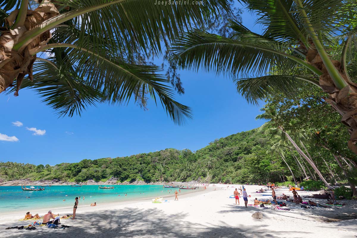 Sunny view of Freedom Beach under a blue sky framed by palm tree fronds with shadows on the white sand.