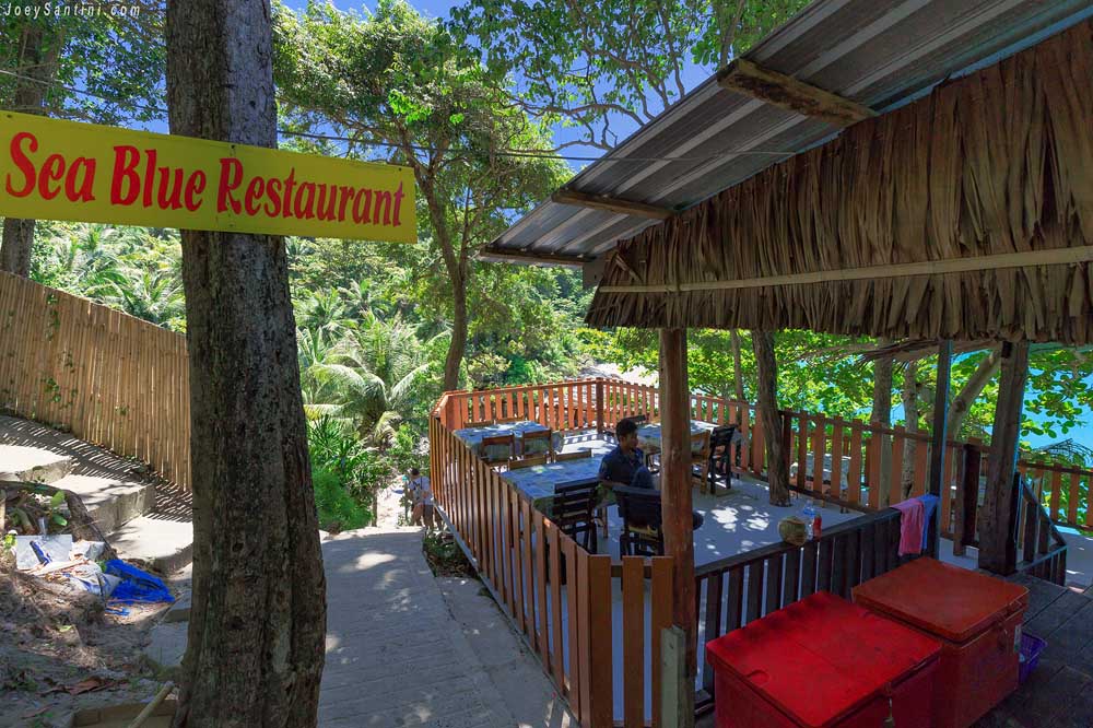 Entrance of Sea Blue Restaurant on the hill overlooking Freedom Beach with a rustic thatched roof.