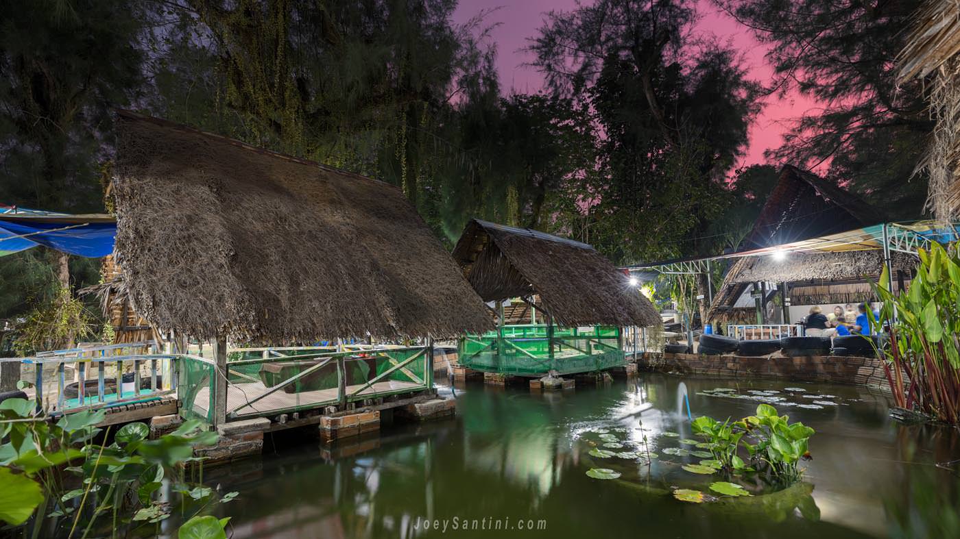 Cabanas with thatched roof surrounded by the trees and water with pink sky in the background