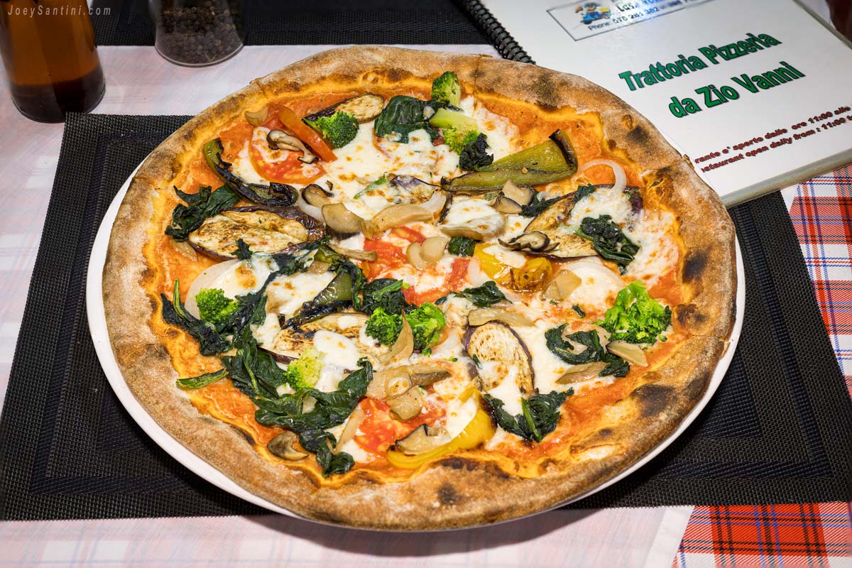 FPhoto of a pizza with green broccili and spinach, red tomatoes, and brown eggplants.
