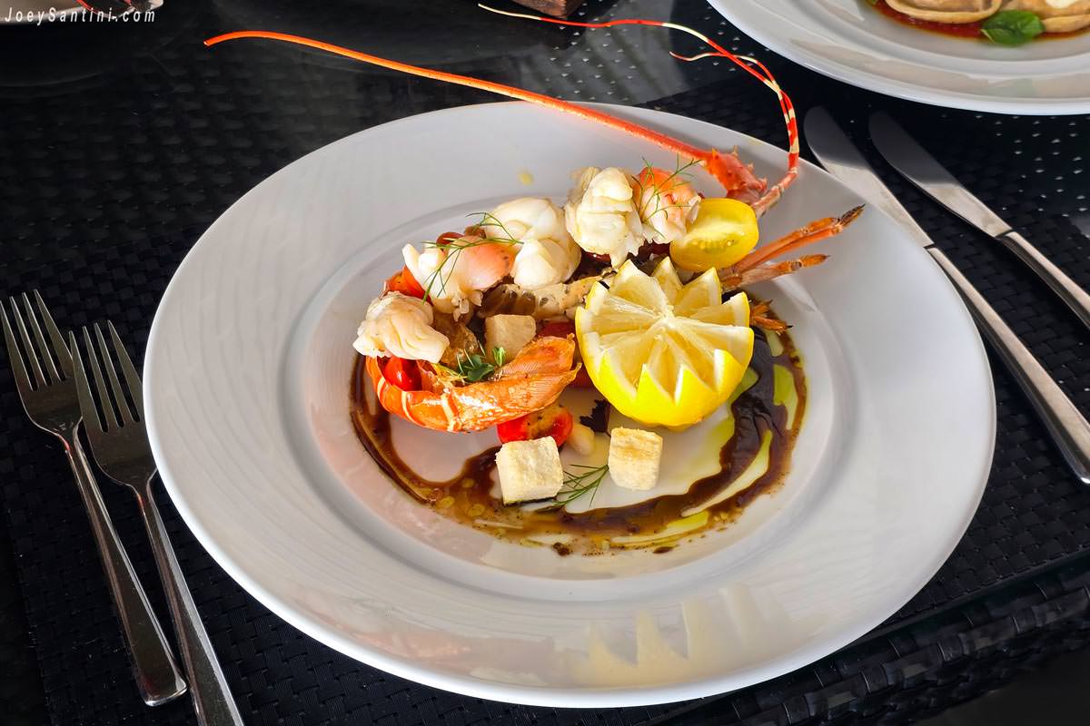 A gourmet lobster salad served in a shell with a carved lemon, croutons, and balsamic reduction drizzle at La Gritta Restaurant.