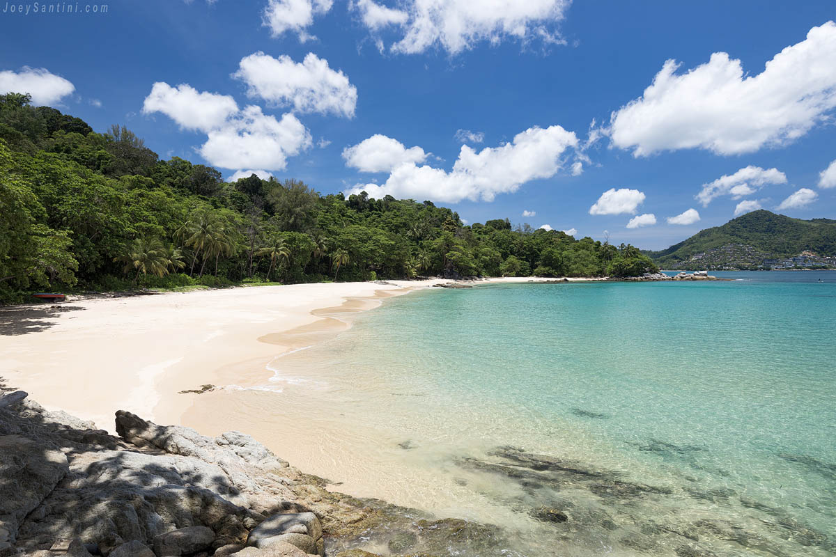 Secluded golden sand shoreline and clear turquoise water of Laem Sing Beach in Phuket under a blue sky with clouds.