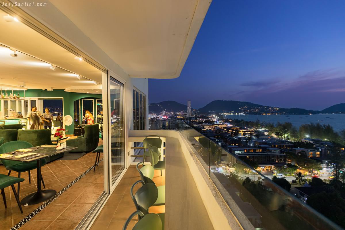 Long balcony seating at Andaman Sky Lounge overlooking the illuminated streets and coastline of Patong at dusk.