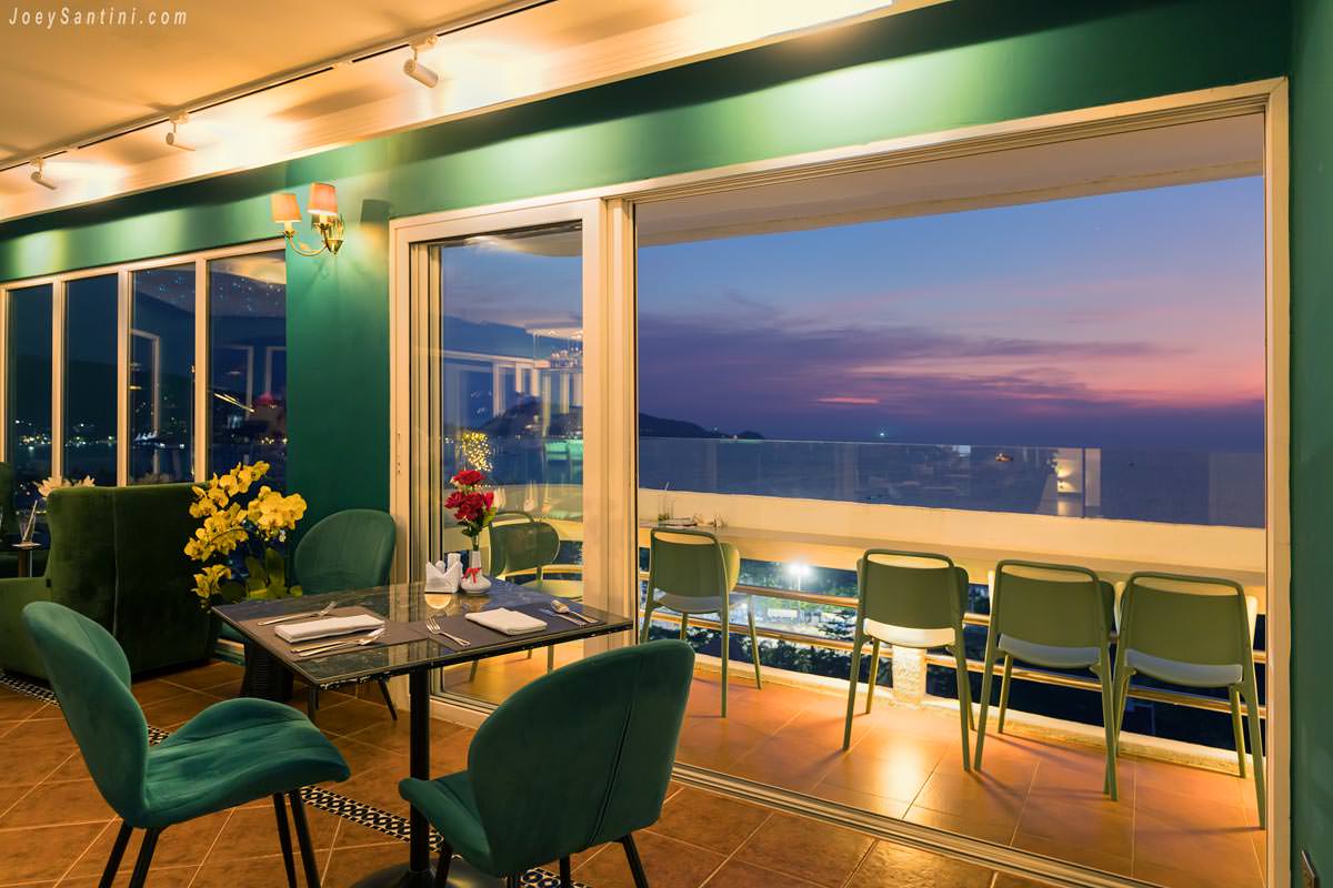 Indoor dining table with velvet green chairs looking out towards a beautiful sunset over the sea at Andaman Sky Lounge.