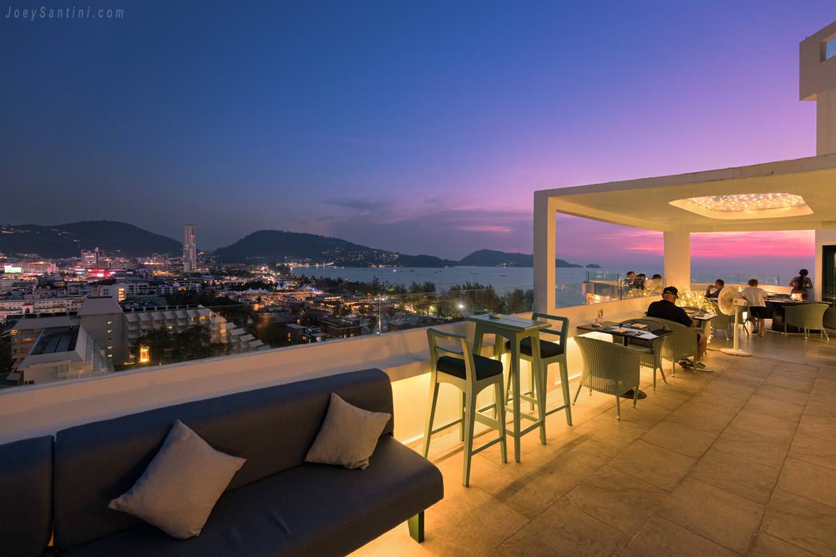 Rooftop terrace at Andaman Sky Lounge in Patong featuring comfortable outdoor seating, high bar stools, and a stunning purple sunset over the bay.