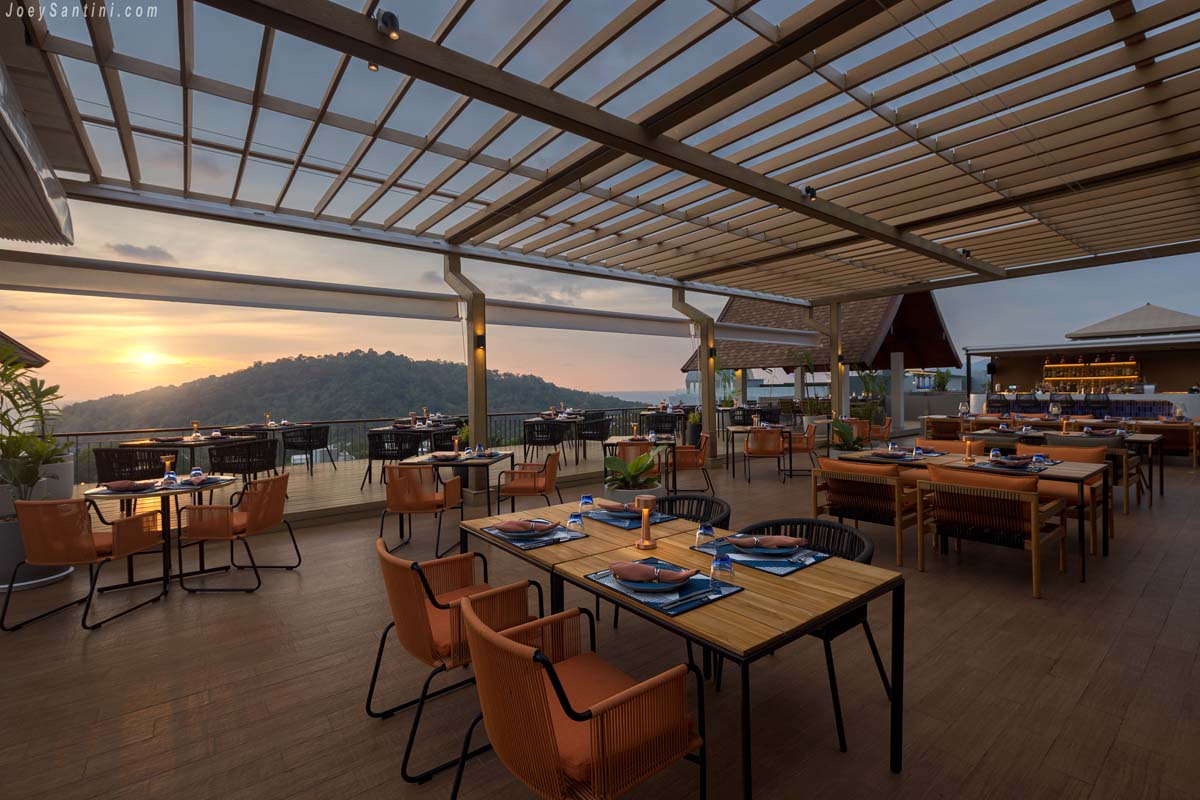 Sizzle Rooftop Bar dining terrace under a wooden pergola during a golden mountain sunset in Phuket.