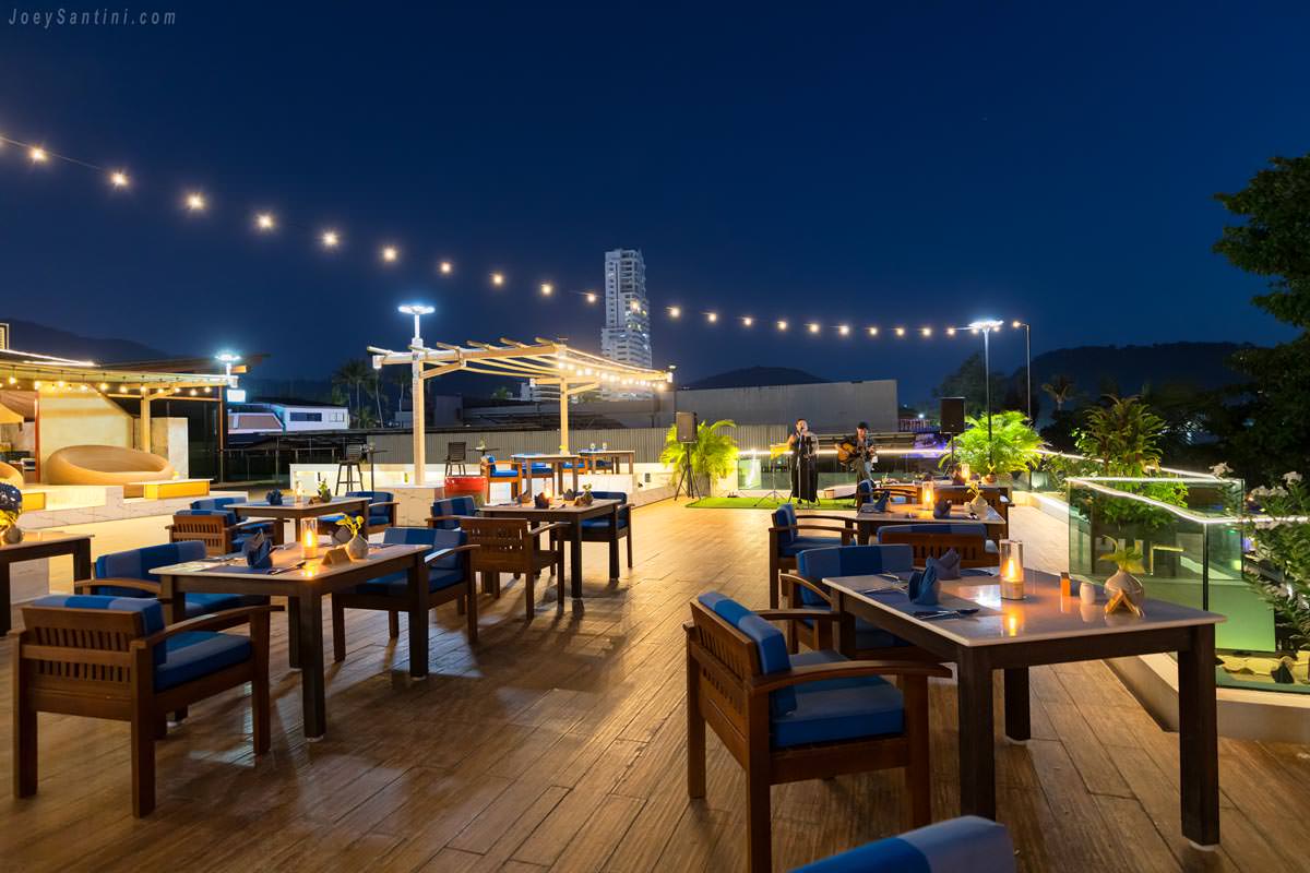 Night atmosphere at The Surface rooftop restaurant at La Flora Resort featuring string lights, dining tables, and live music.