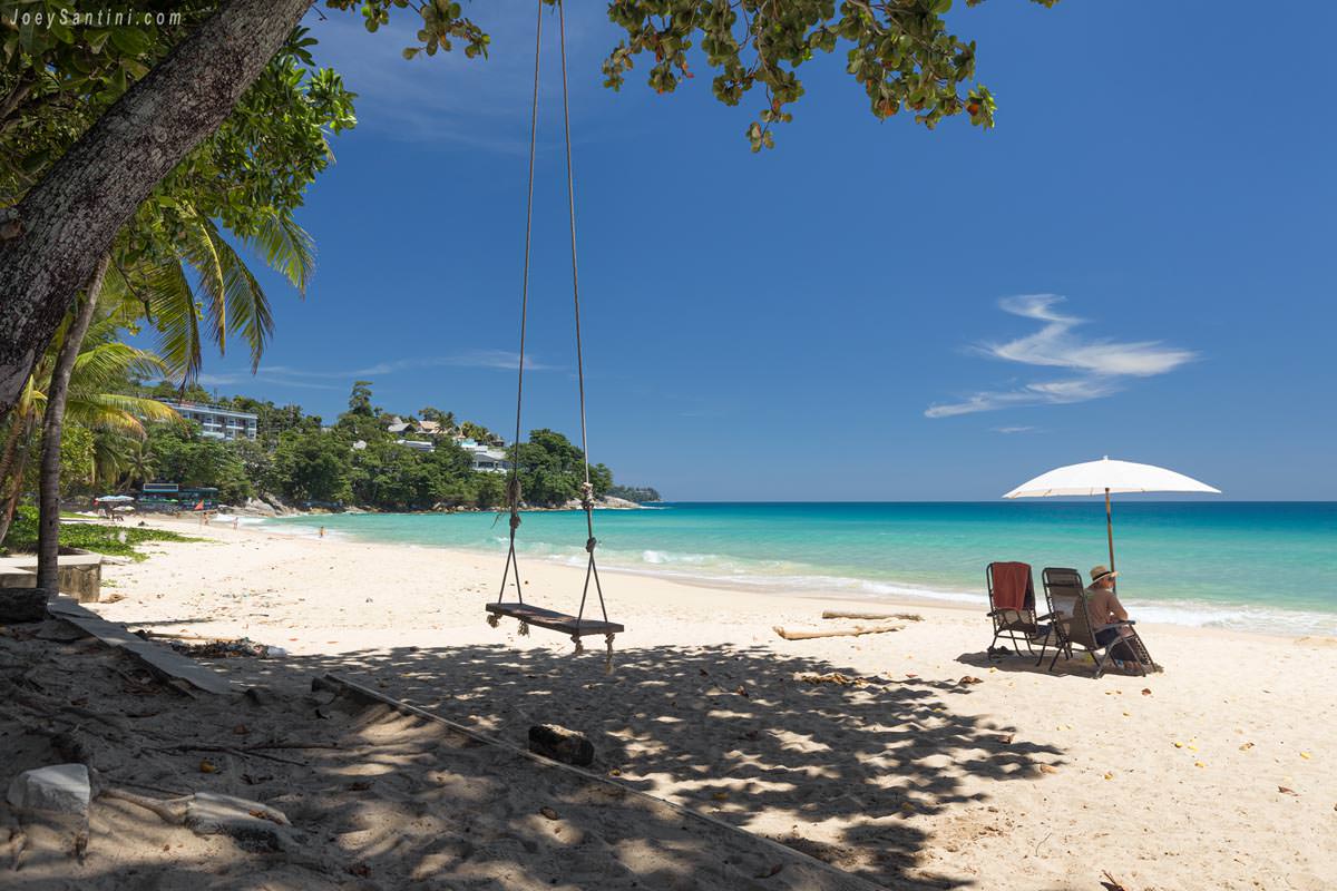 Showing white sand of the beach and green trees with blue sky in the background