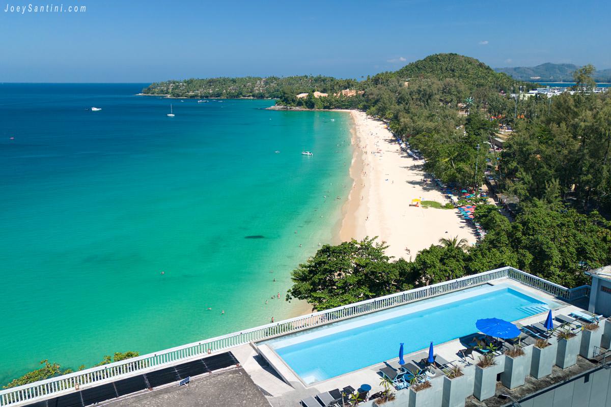 High-angle view of the rooftop infinity pool at Norn Talay Surin Beach Phuket overlooking the turquoise ocean and white sands of Surin Beach.