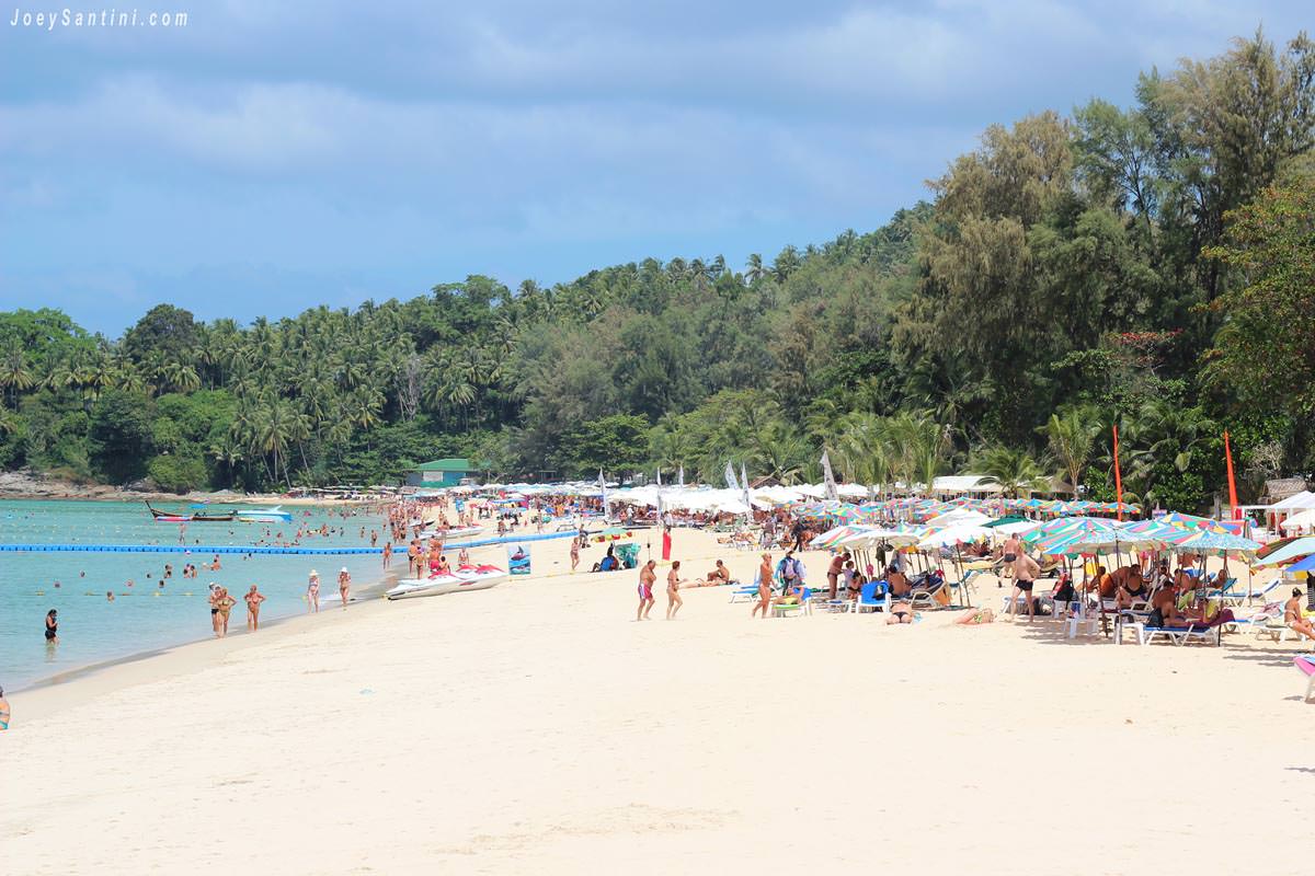 Crowded Surin Beach in Phuket during February 2012 with rows of beach umbrellas, sun loungers, and a long floating pontoon in the sea.