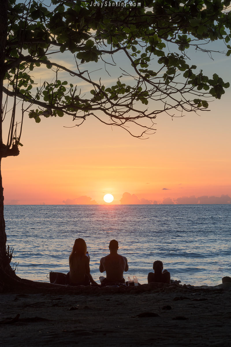Silhouette of people sitting on the sand watching the sunset over the ocean at Surin Beach, Phuket.