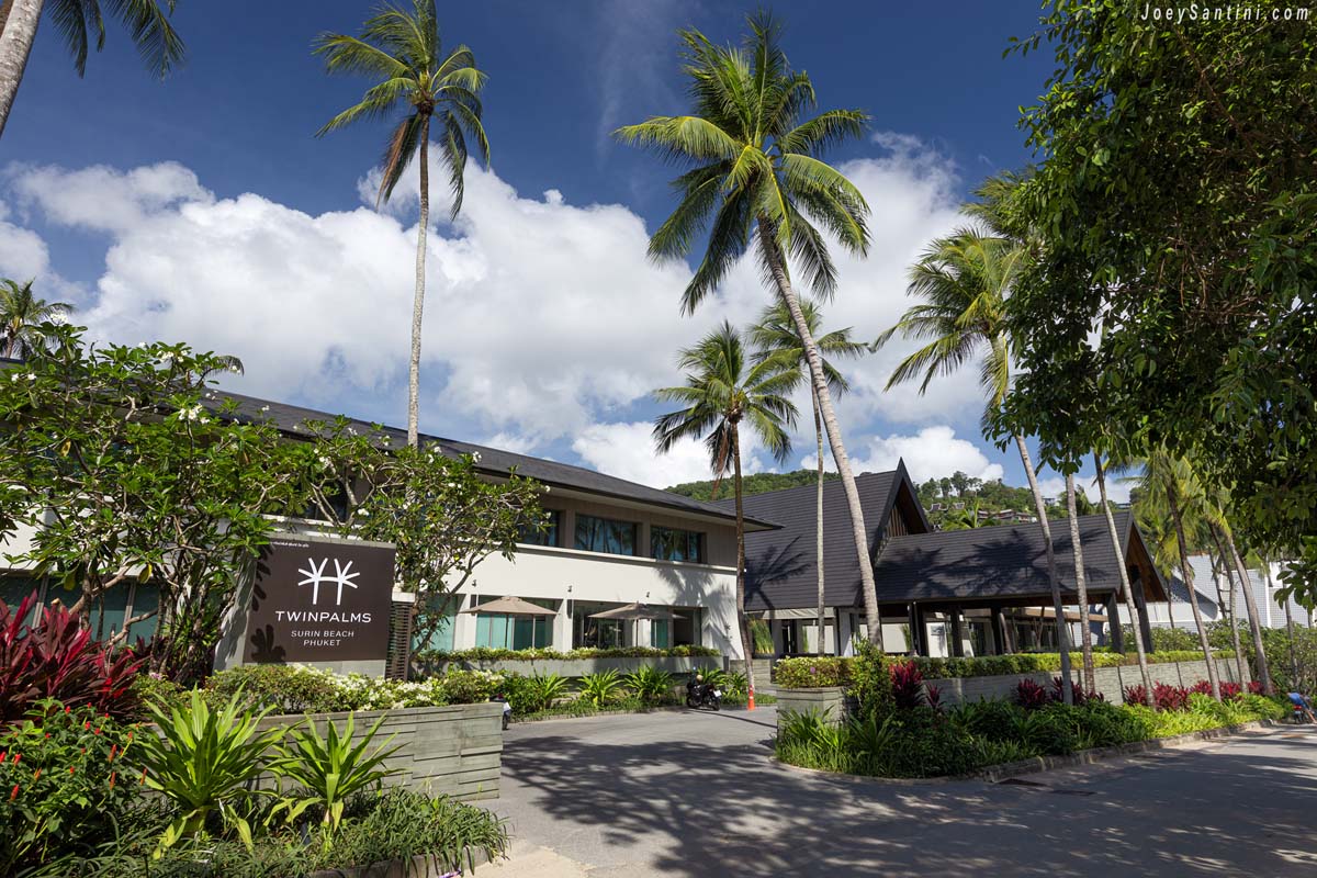 The luxury entrance and sign of Twinpalms Phuket Resort near Surin Beach surrounded by tall palm trees.