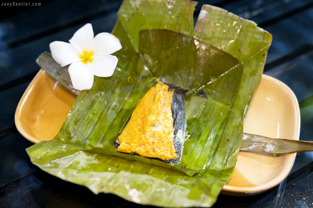 Authentic Hor Mok steamed fish curry mousse served in a banana leaf packet with a white frangipani flower