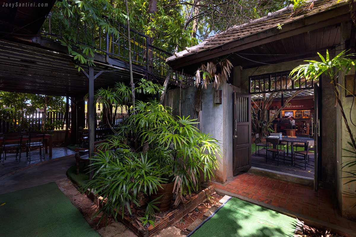 Wooden pavilion doorway leading to tropical courtyard dining section at Krua Praya Phuket
