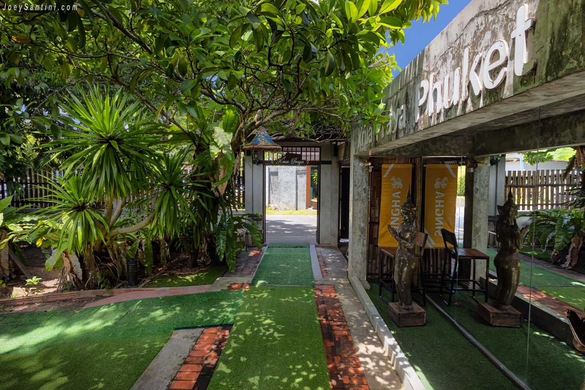 Green turf walkway passing concrete signage into the garden dining space at Krua Praya Phuket