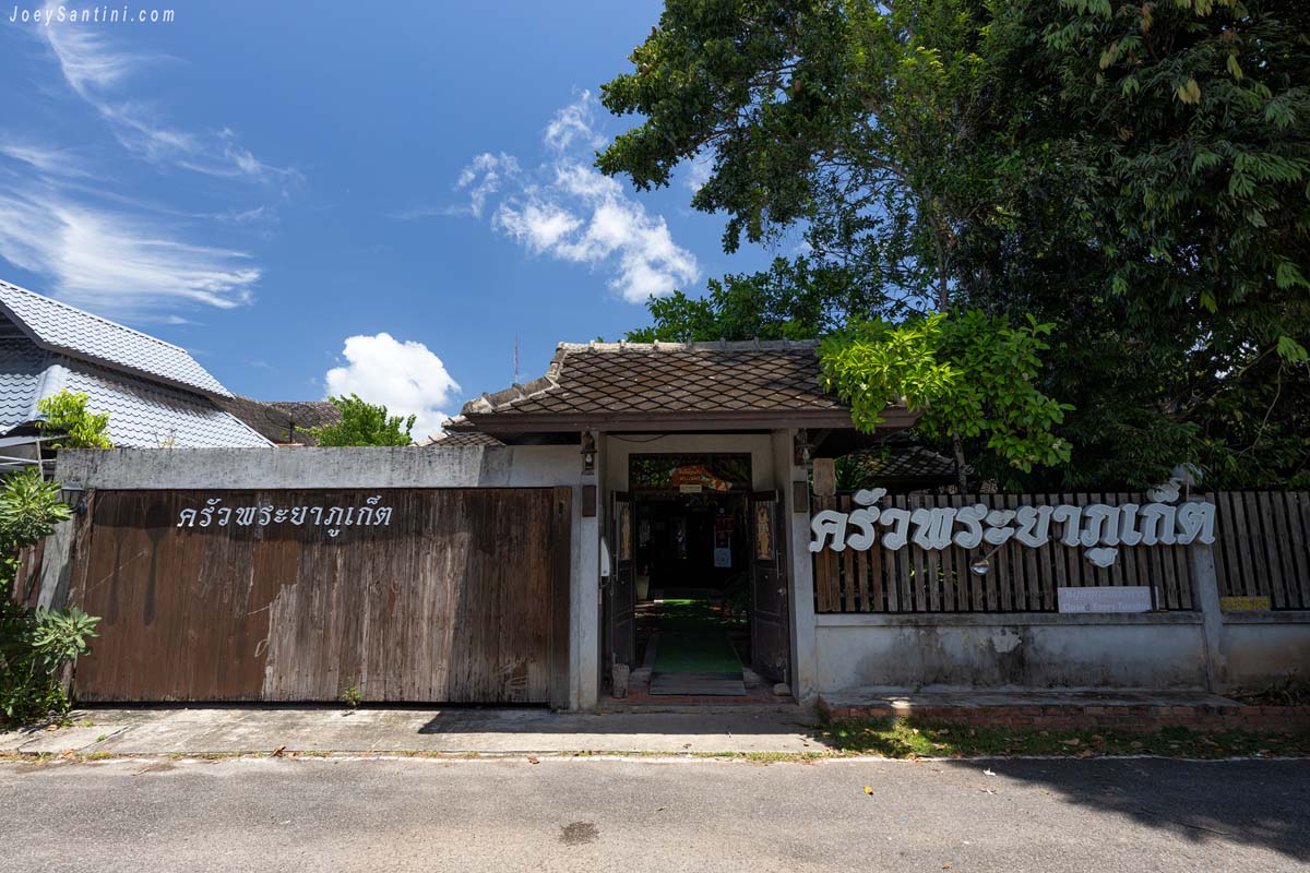 Rustic wooden gate and Thai script signage at the entrance of Krua Praya Phuket