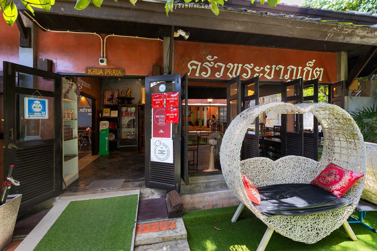Krua Praya Phuket entrance with Michelin Bib Gourmand plaques and white woven lounge chair