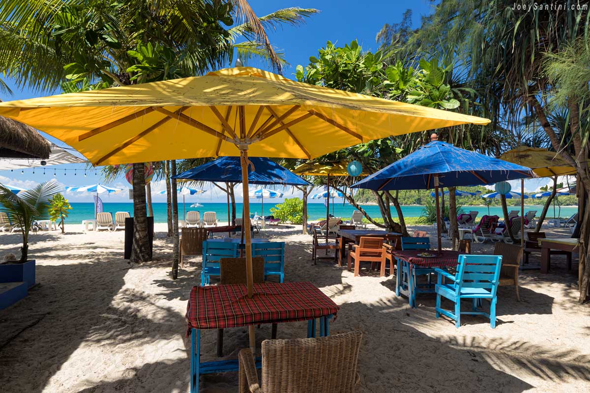 Colorful wooden tables under large yellow umbrella on sand at layan beach phuket