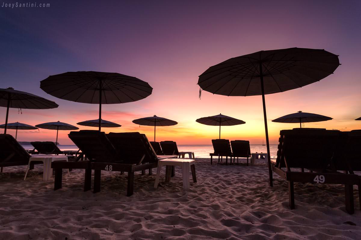 beach umbrellas and loungers on sand under purple twilight sky at layan beach phuket