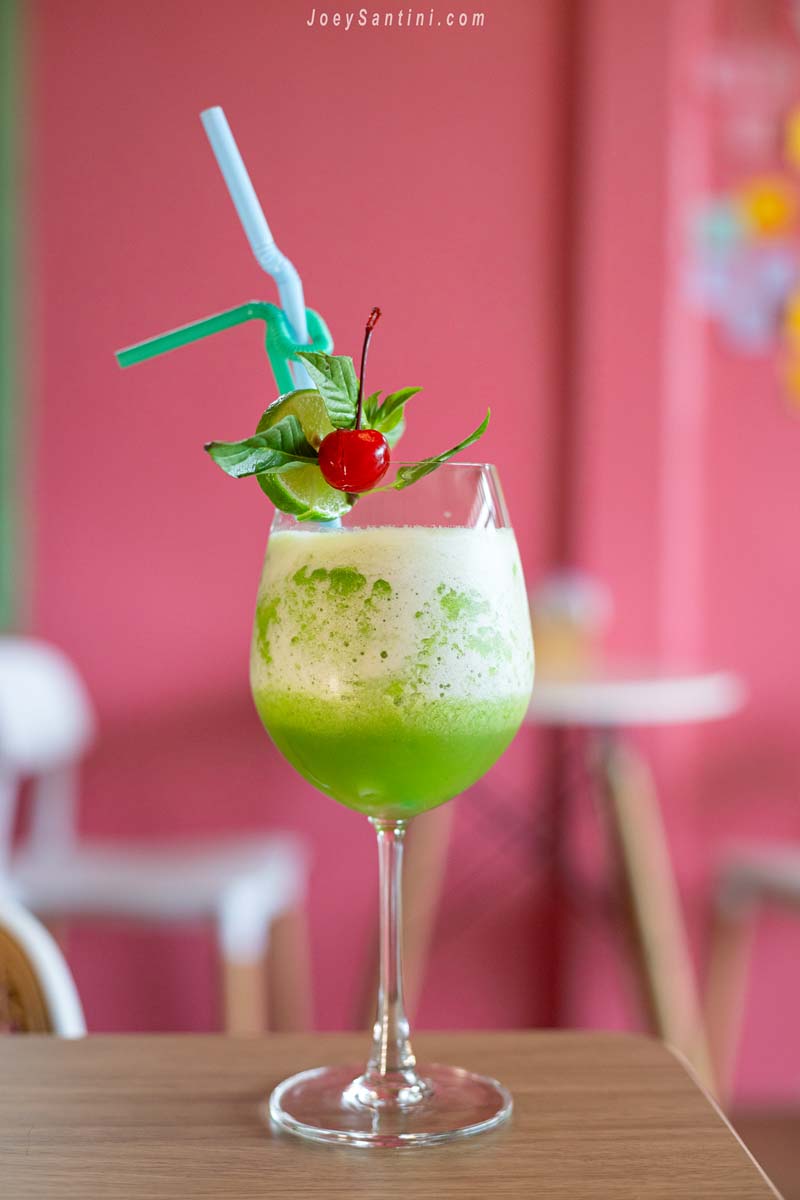 refreshing green mint and lime smoothie garnished with a cocktail cherry against a pink wall at sweet come phuket