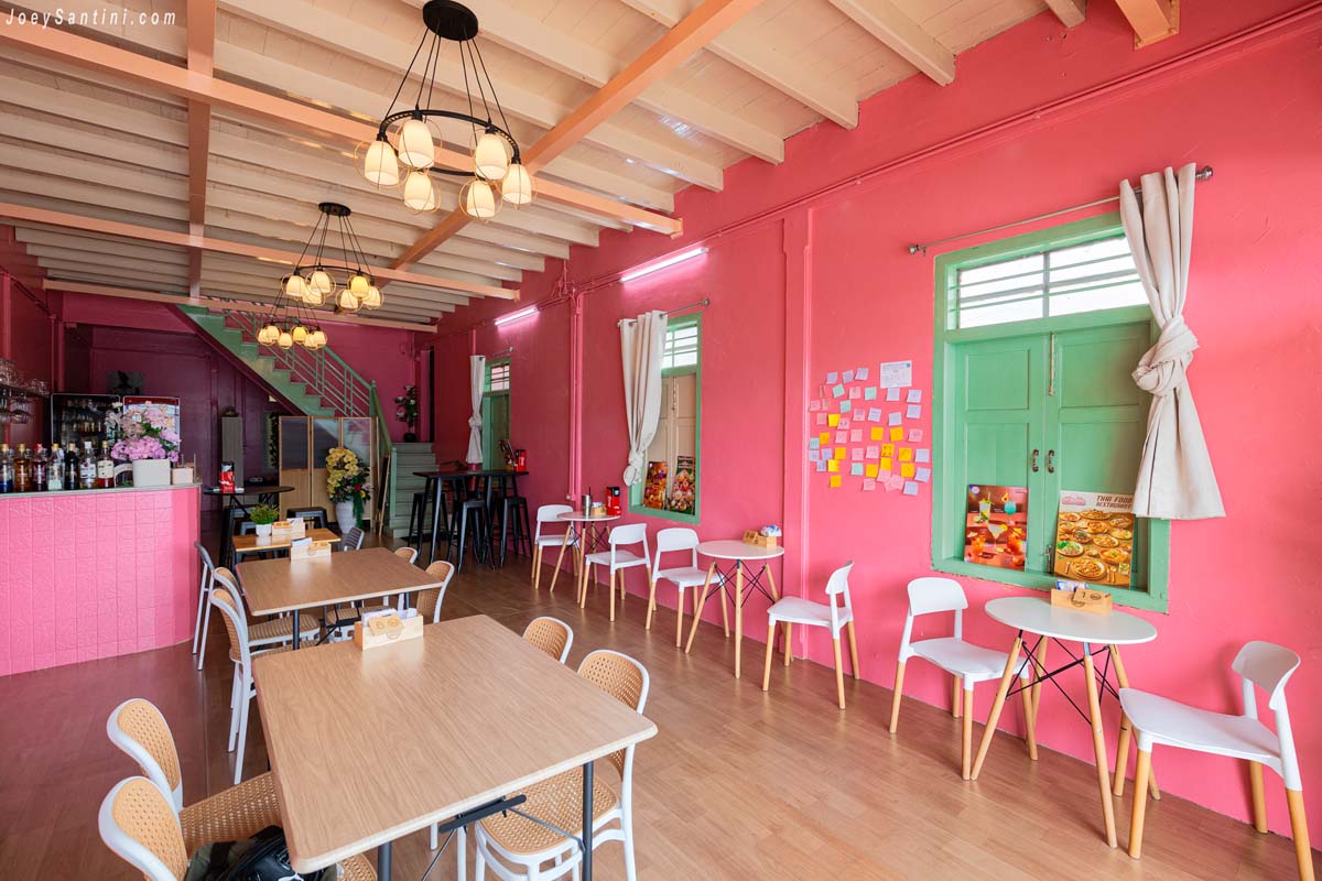 bright pink dining area with wooden tables and Sino Portuguese teal windows at sweet come phuket