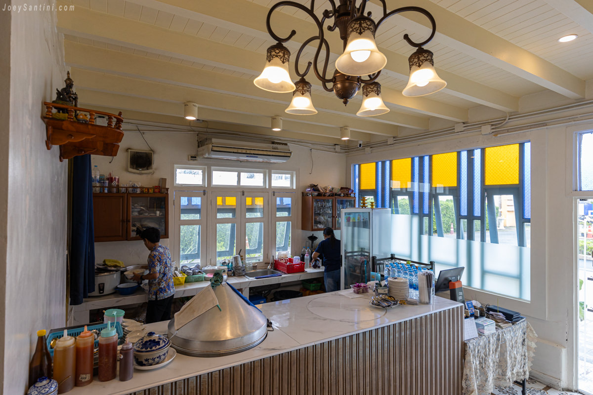 Interior counter area of Thai Mueang Restaurant in Phuket featuring a service station staff working stained glass windows and an ornate chandelier