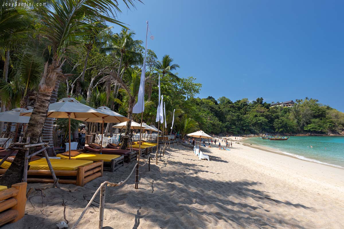 Wooden sun loungers with yellow cushions and white umbrellas on the sandy beach of Banana Beach in Phuket