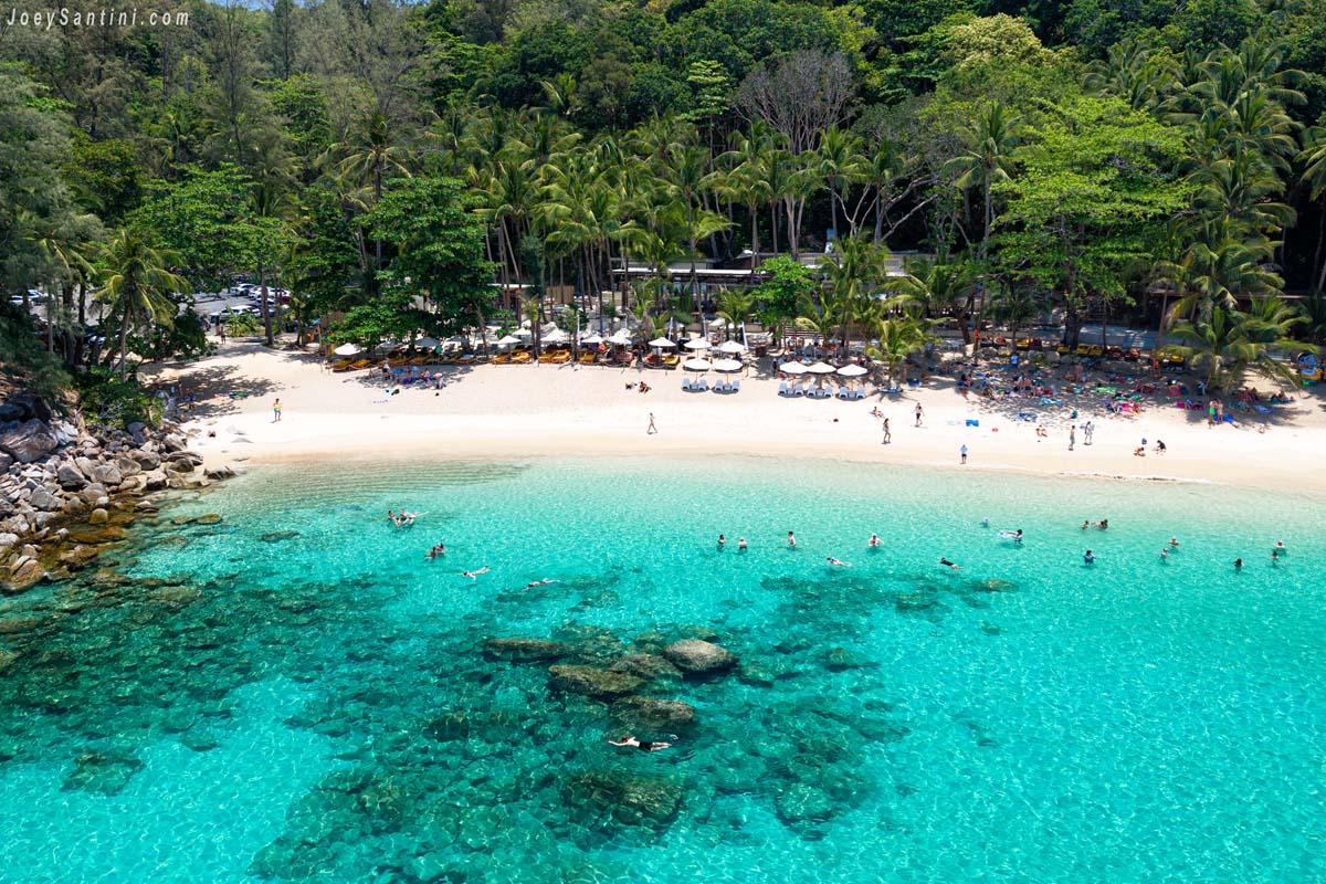 Aerial view of coral reefs, swimmers, and beachfront facilities nestled under the trees at Banana Beach