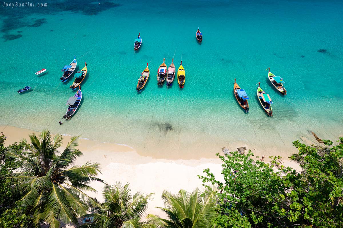 Top-down drone view of multiple longtail boats anchored neatly on the shallow blue waters of Banana Beach