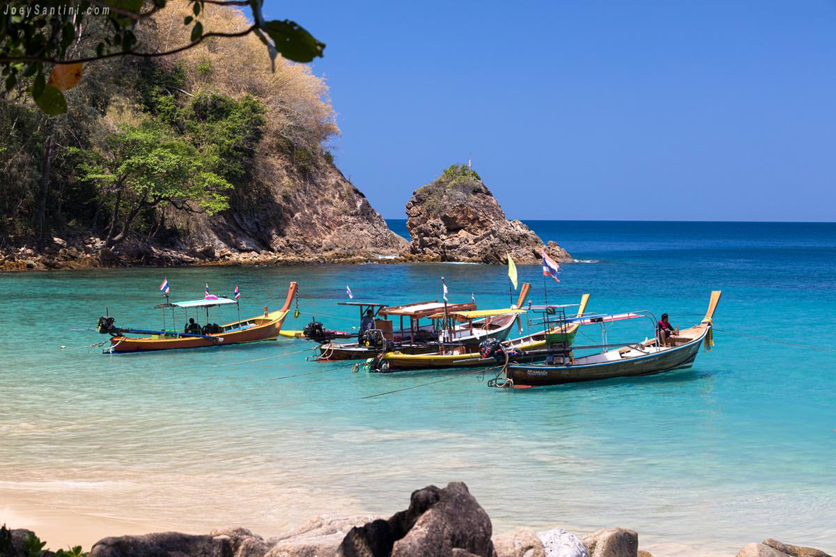Traditional longtail boats moored together in the crystal-clear water near a rocky islet at Banana Beach Phuket
